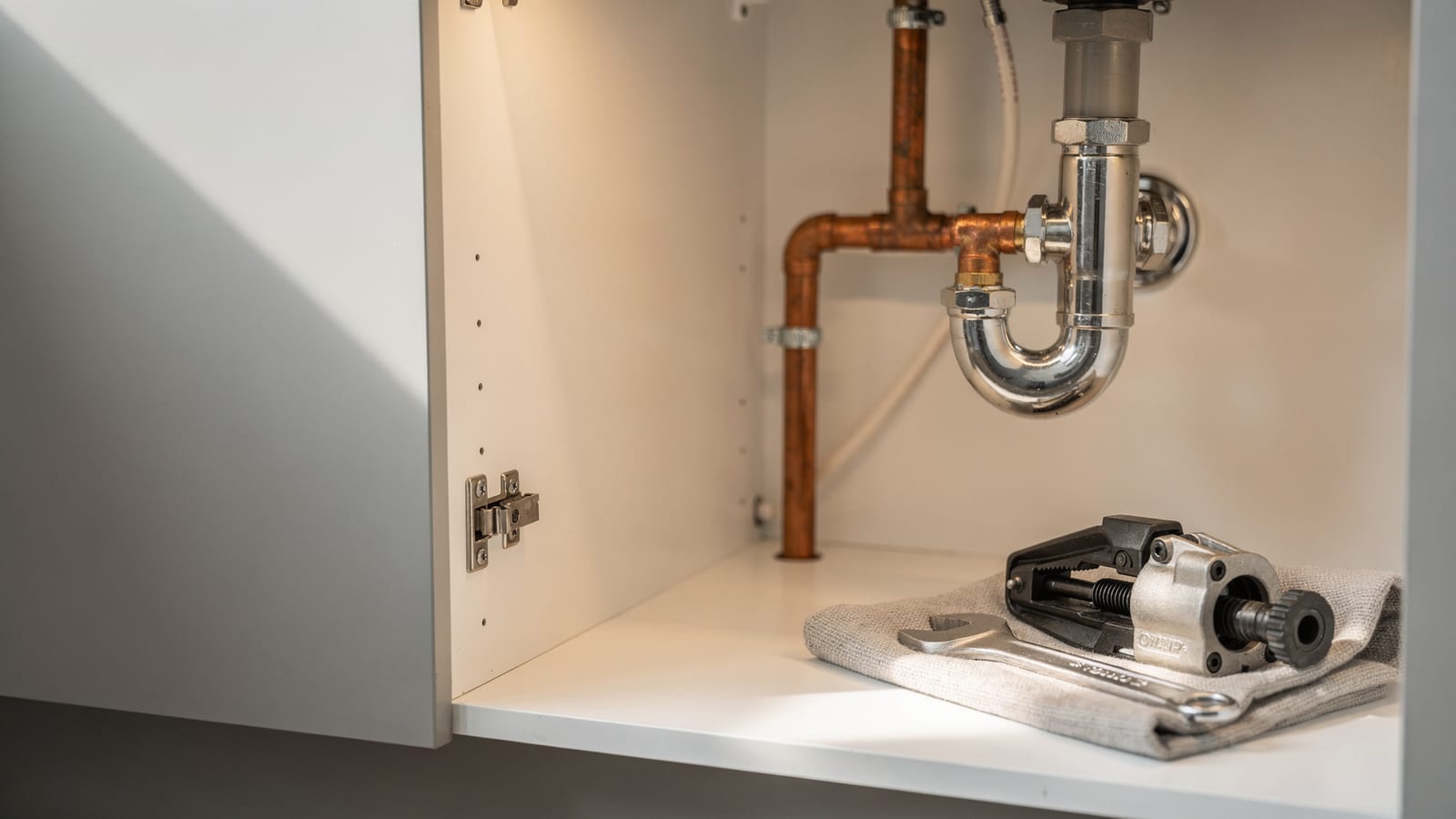 Neatly installed copper and chrome plumbing under a sink, tools resting on a cloth